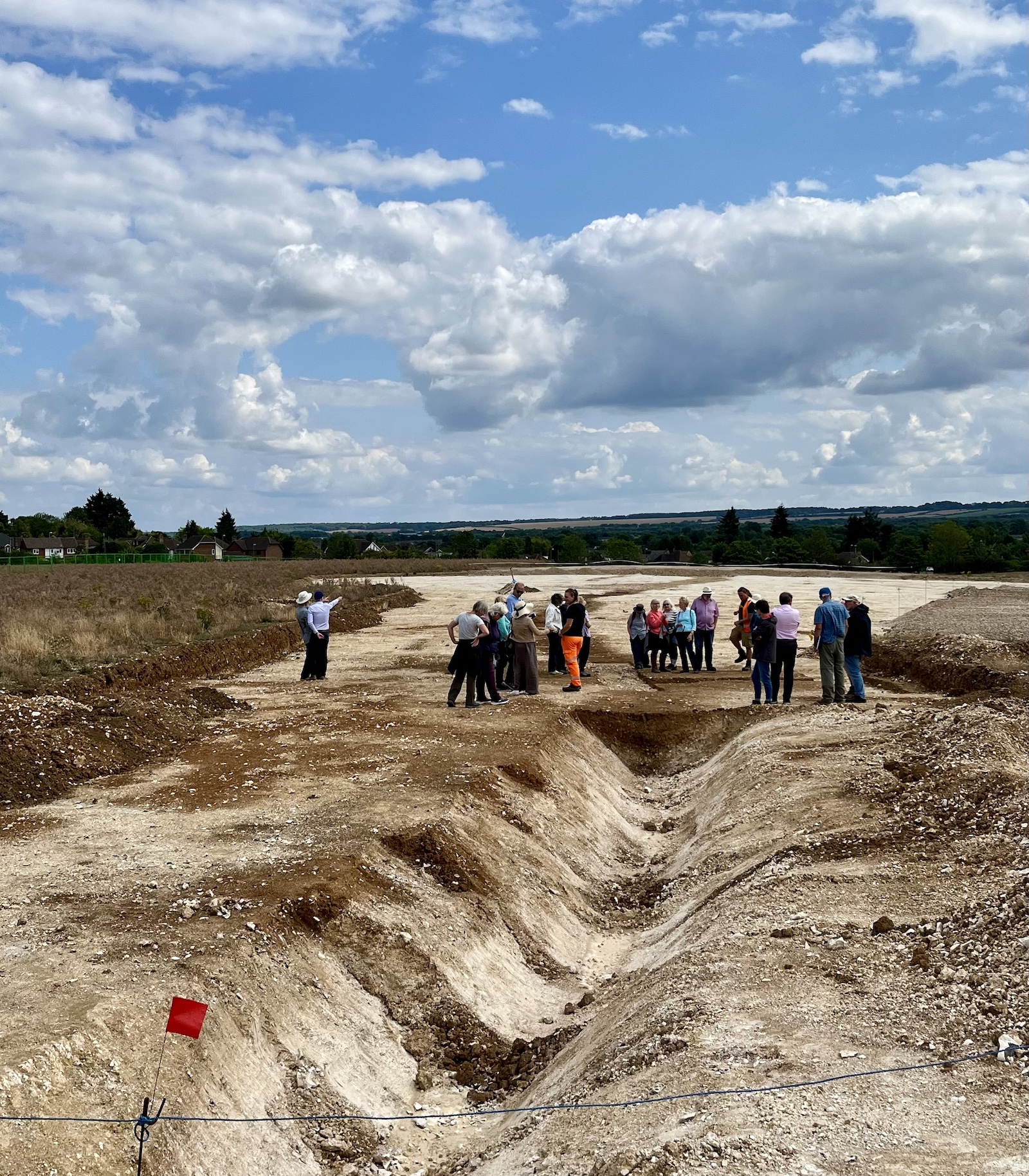 A group of people wearing hats gathered at an archaeology site on a bright sunny day